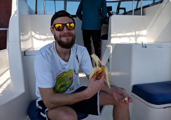 A man in a white shirt and sunglasses holding a banana on a boat