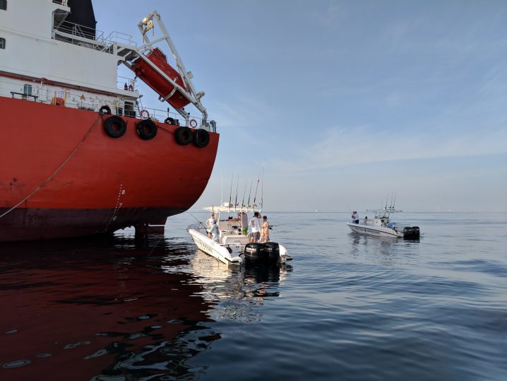 Two charter boats at the back of a red Fujairah oil tanker fishing for bottom fish