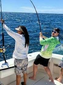 Two anglers actively reeling in their lines while fishing on a sunny day in open waters, showcasing the excitement of the catch.
