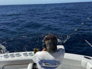 A young angler is actively fishing on a sportfishing boat, casting into the deep blue waters, showcasing the excitement of offshore fishing.