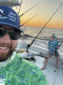 Two anglers enjoying a sunset fishing trip on a sport fishing boat, with one actively reeling in a line.