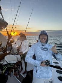 A group of anglers enjoying a vibrant sunset while fishing on a boat, with one angler giving a thumbs up, showcasing the excitement of the fishing experience.