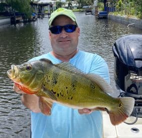 Angler proudly displaying a vibrant Peacock Bass while fishing in a scenic canal setting.