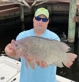 Angler proudly displaying a large Tilapia caught at a local fishing spot, showcasing a successful day on the water.