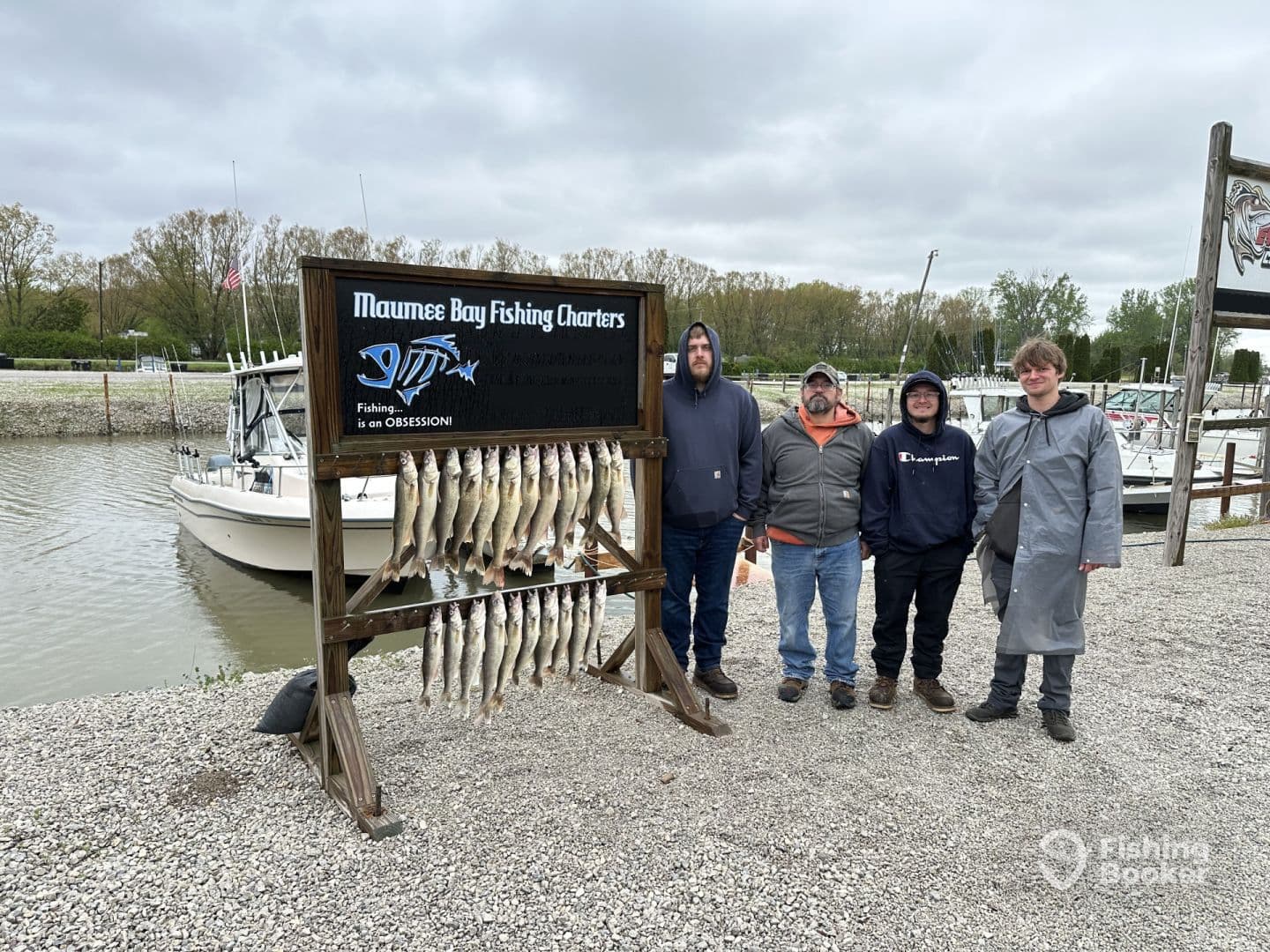 A group of four anglers proudly posing by a catch board displaying multiple Walleye at Maumee Bay Fishing Charters, with a boat visible in the background.