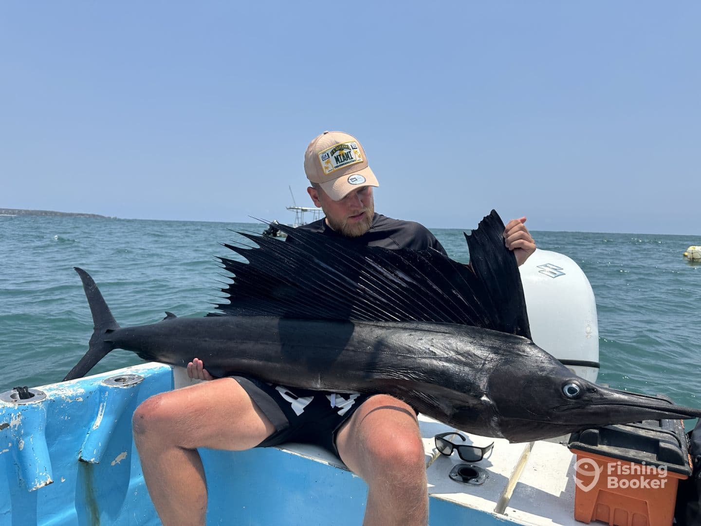 An angler proudly displaying a large Sailfish while seated in a small boat, showcasing a successful deep-sea fishing trip.
