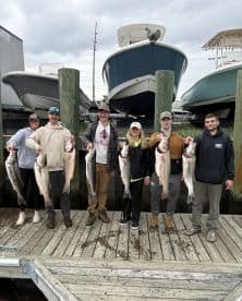 A group of anglers proudly displaying their catch of striped bass at the dock, showcasing a successful fishing trip.