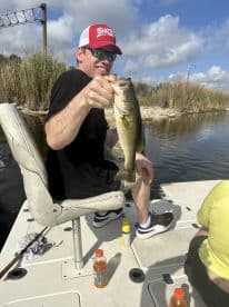 Angler proudly displaying a large Largemouth Bass while fishing from a boat in a scenic waterway.