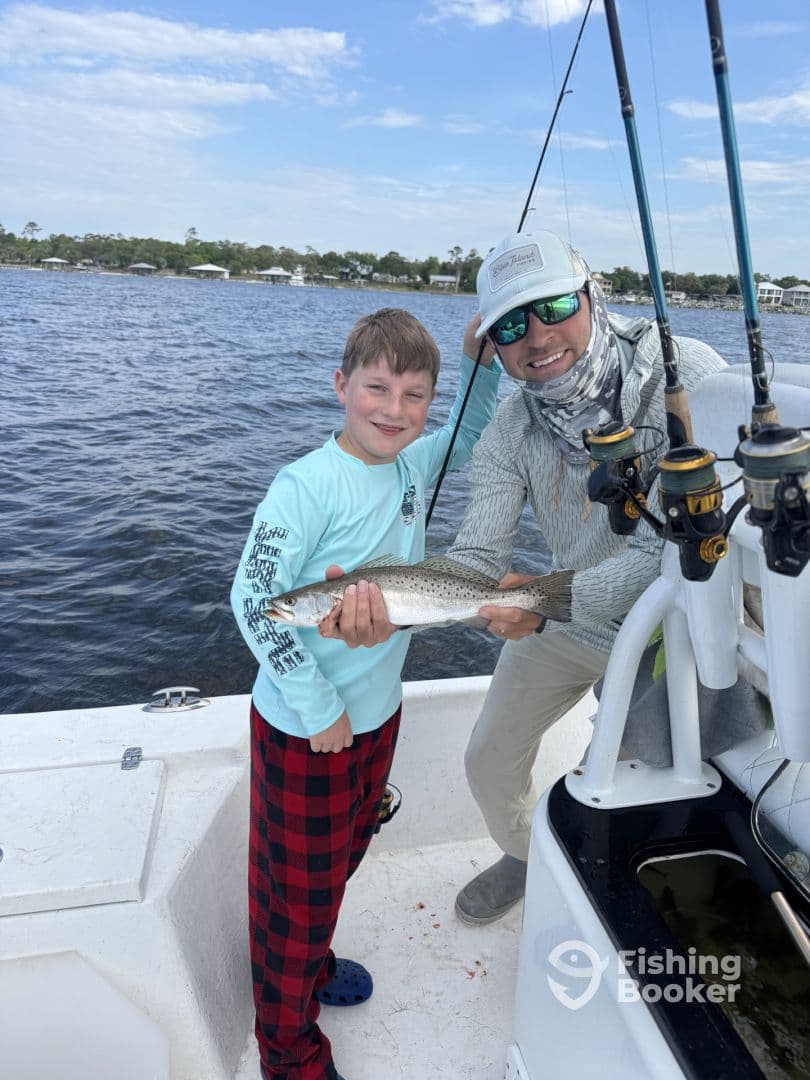 A young angler and a guide proudly displaying a Speckled Trout on a fishing boat, showcasing a successful day on the water.