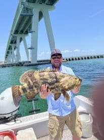 Angler proudly displaying a large Goliath Grouper while fishing near a bridge in a coastal environment.