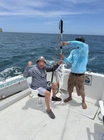 Angler celebrating with a large fish on a sport fishing boat, showcasing the excitement of deep-sea fishing.
