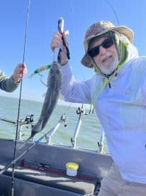 An angler proudly displaying a caught fish while fishing on a boat, showcasing a sunny day on the water.