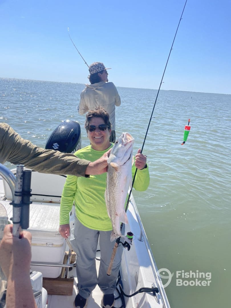 Angler proudly displaying a large Speckled Trout while fishing on a boat in calm waters.
