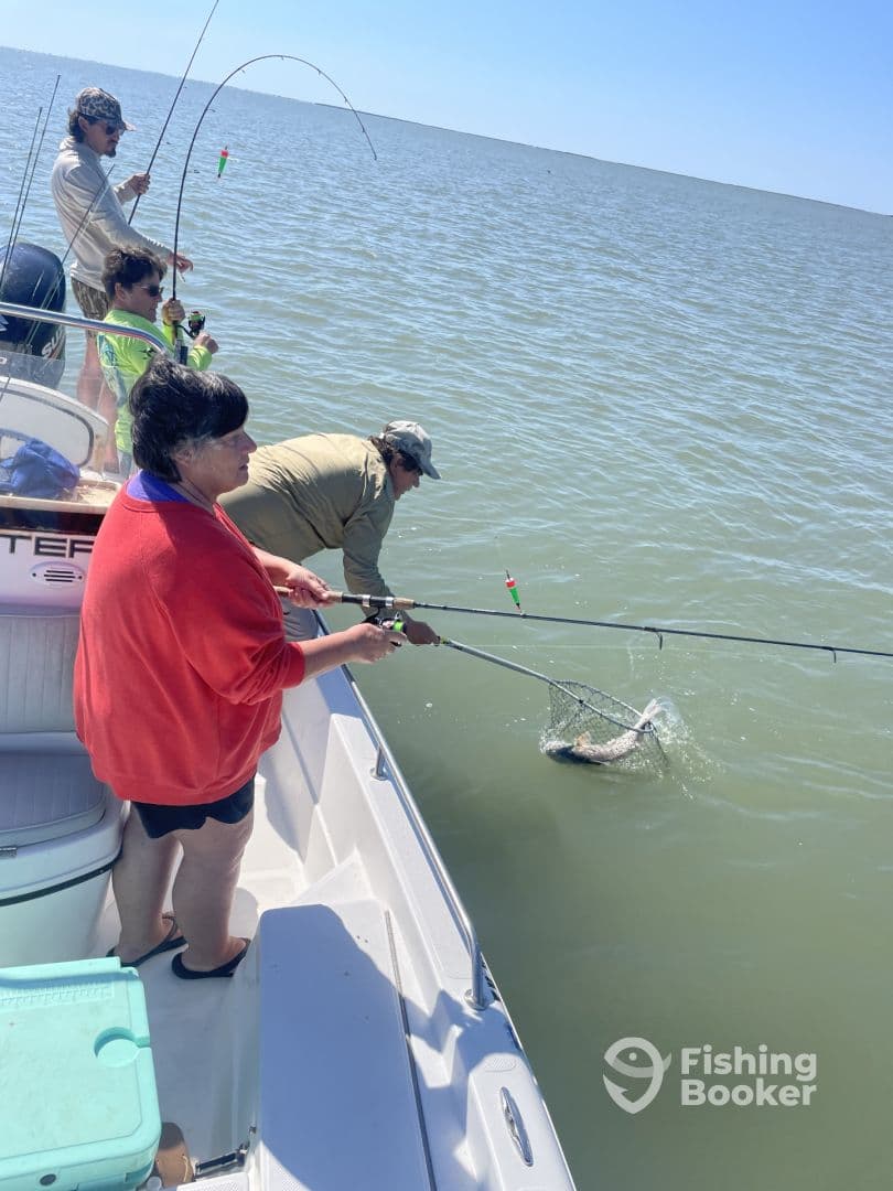 A family fishing trip in progress, with an angler using a net to catch a fish while others assist from the boat.