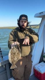 Angler displaying a Flounder while fishing on a boat, showcasing a successful catch in a scenic waterway.