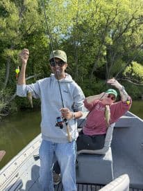 Two anglers proudly displaying their catches of bass while fishing on a serene lake, surrounded by lush greenery.