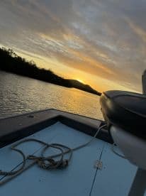 A serene sunset view from the bow of a fishing boat, showcasing the calm waters and surrounding landscape.