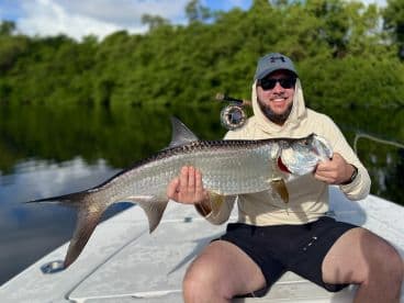 Angler proudly displaying a large Tarpon while fishing on a calm river, showcasing a successful catch during a guided trip.