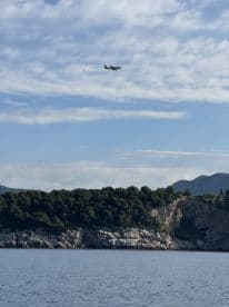 An airplane flying over a coastal landscape, with rocky cliffs and greenery visible in the background.