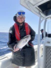 Angler holding a sizable fish while aboard a fishing boat in open waters, showcasing a successful catch during a deep-sea fishing trip.