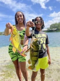 A mother and son proudly displaying their catches of Largemouth Bass and another species at a scenic lake, showcasing a fun family fishing day.