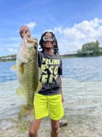 Young angler proudly displaying a large Largemouth Bass while fishing at a scenic lake.