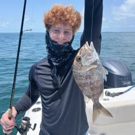 A young angler proudly displaying a freshly caught Snapper while fishing on a boat in clear waters.