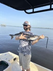 Angler proudly displaying a large Black Drum while fishing from a boat in calm waters.