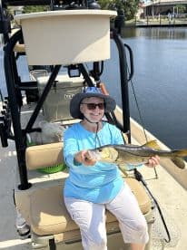 An angler proudly displaying a Snook while seated on a boat, enjoying a sunny day on the water.