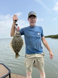 An angler proudly displaying a large Flounder while fishing in a coastal waterway.