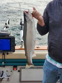 Angler proudly displaying a freshly caught Salmon while fishing on a boat, showcasing the excitement of a successful catch.