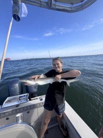 Young angler proudly displaying a caught shark while aboard a fishing boat in a coastal waterway.