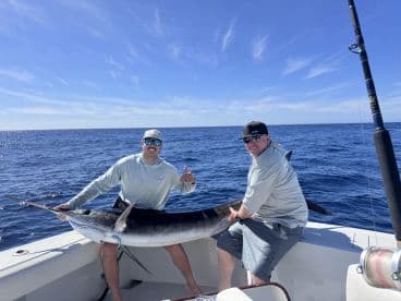Two anglers proudly displaying a large Marlin on a sport fishing boat, enjoying a successful day on the open ocean.