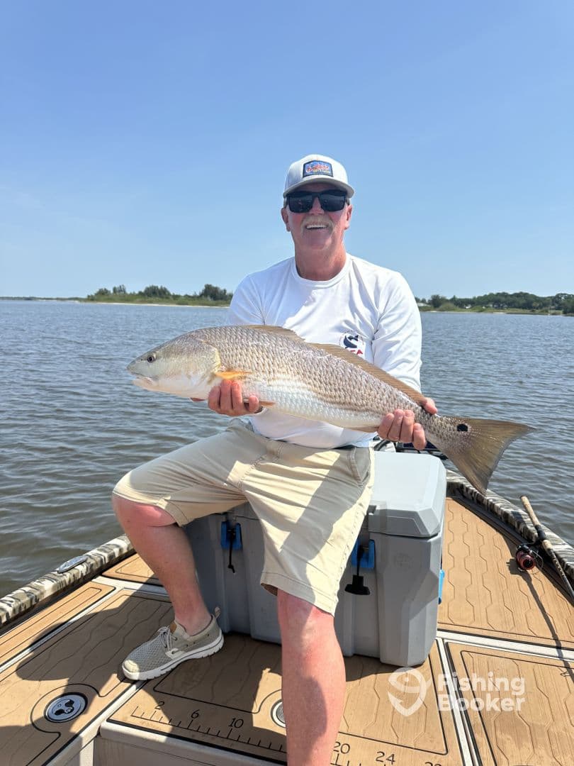 An angler proudly displaying a large Redfish while seated on a boat, enjoying a sunny day on the water.
