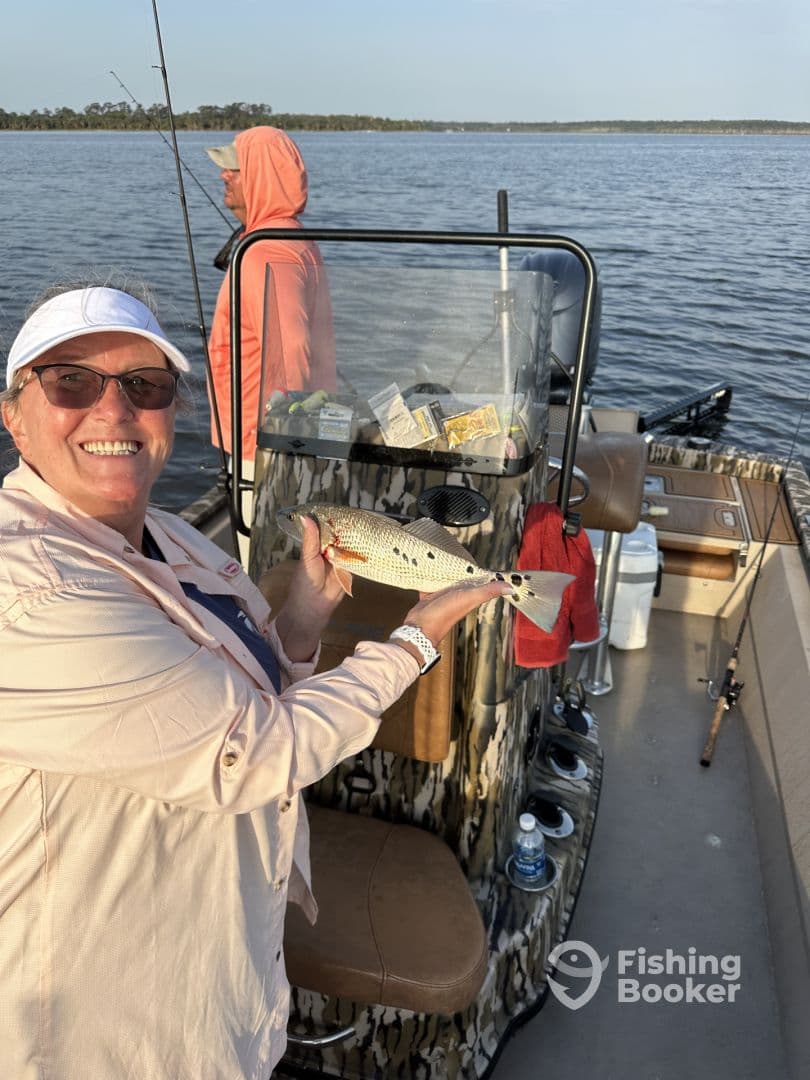 An angler proudly displaying a Speckled Trout while fishing on a boat in a serene waterway.