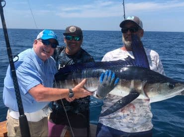 Three anglers proudly displaying a large Sailfish while fishing offshore, showcasing the excitement of deep-sea fishing.