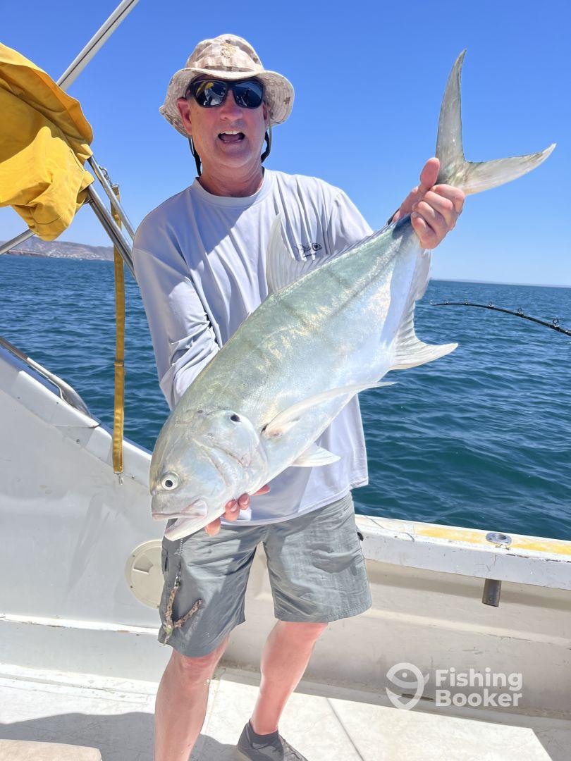 An angler proudly displaying a large Jack Crevalle while fishing on a boat in clear blue waters.