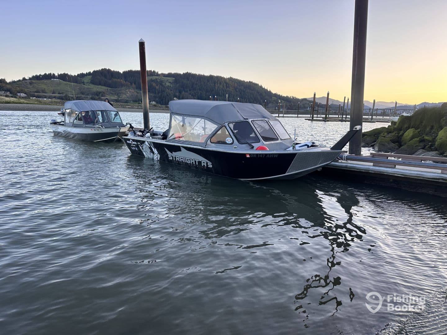 Two fishing boats docked in a serene waterway, showcasing their sleek designs against a backdrop of lush hills.