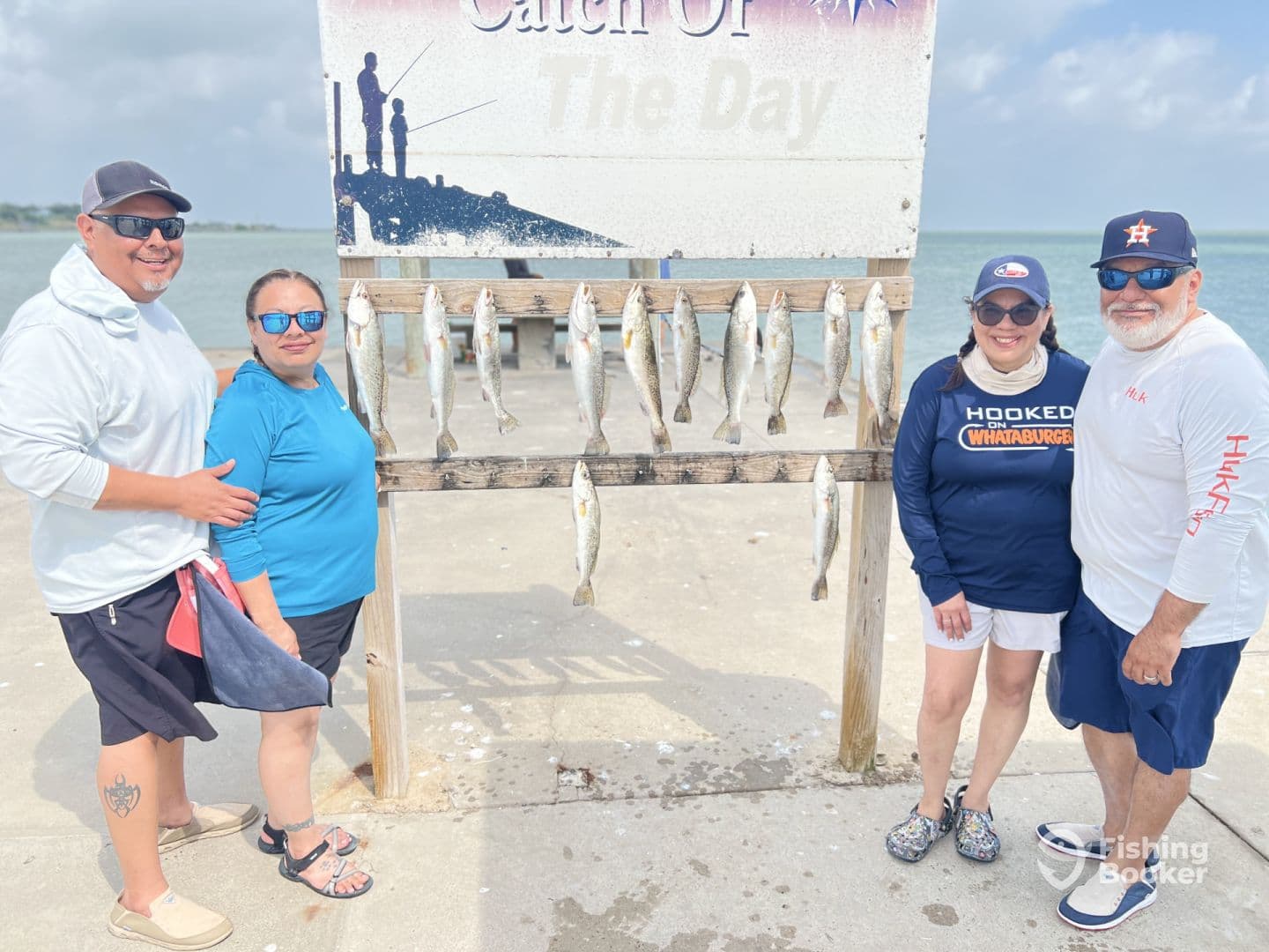 A group of four anglers proudly posing in front of a catch board displaying several Speckled Trout after a successful fishing trip.