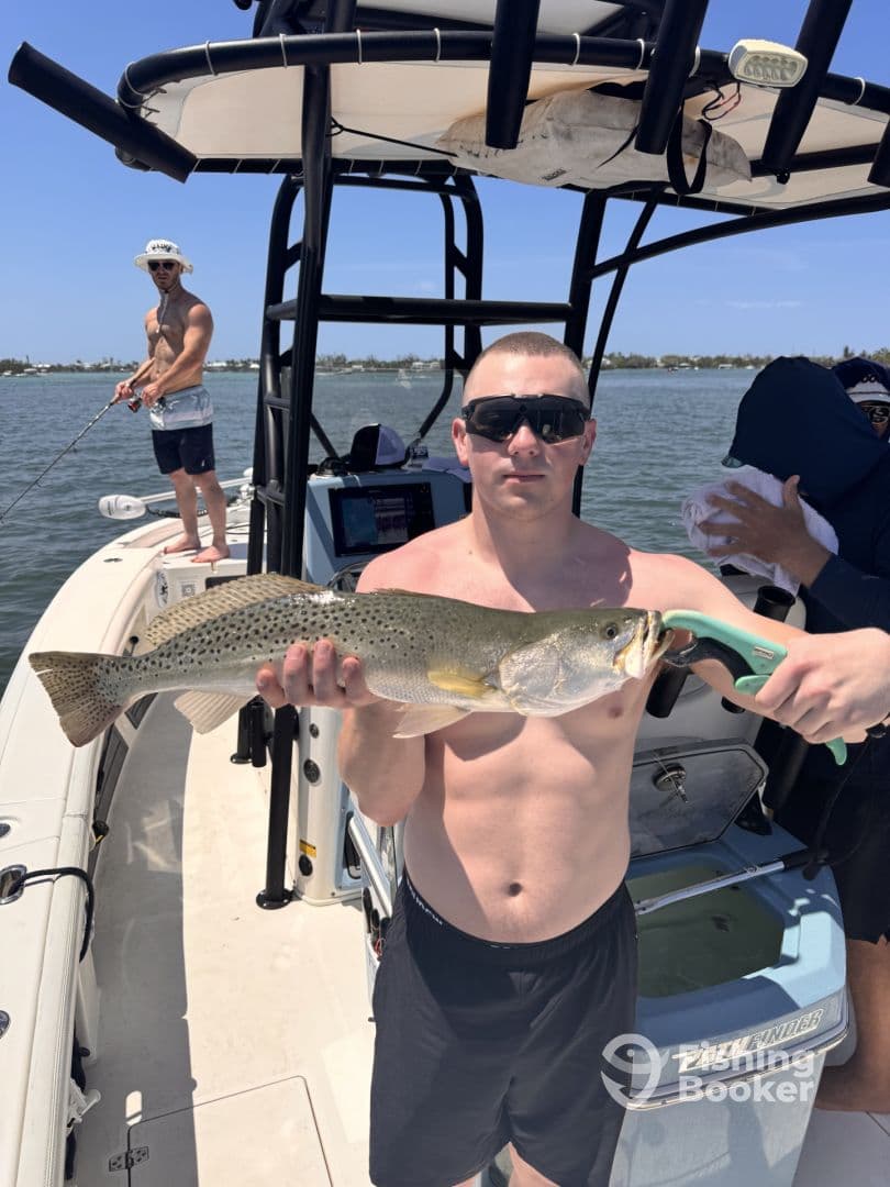 Angler proudly displaying a large Speckled Trout while fishing on a boat in a coastal waterway.