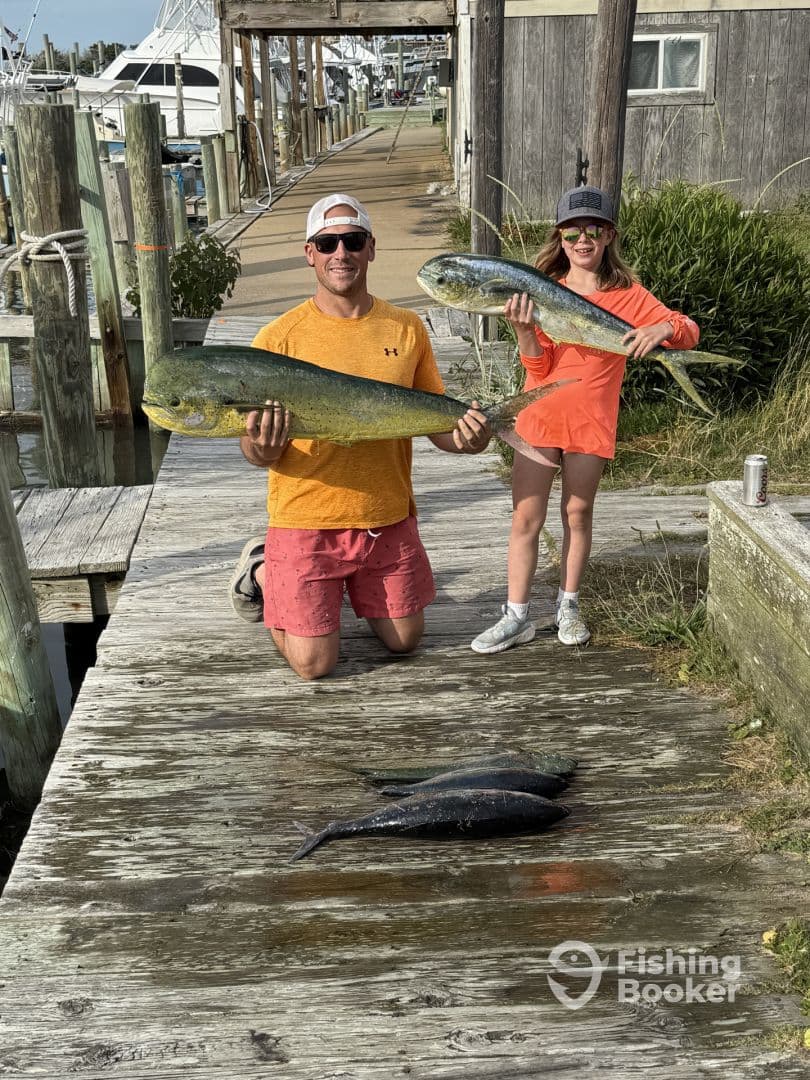 A proud father and daughter duo displaying their catch of Mahi Mahi on the dock after a successful fishing trip.