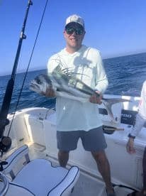 Angler proudly displaying a large Roosterfish aboard a fishing boat, enjoying a successful day on the water.