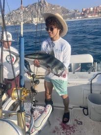 A young angler proudly displaying a large fish aboard a boat in Cabo San Lucas, showcasing the excitement of a successful fishing trip.