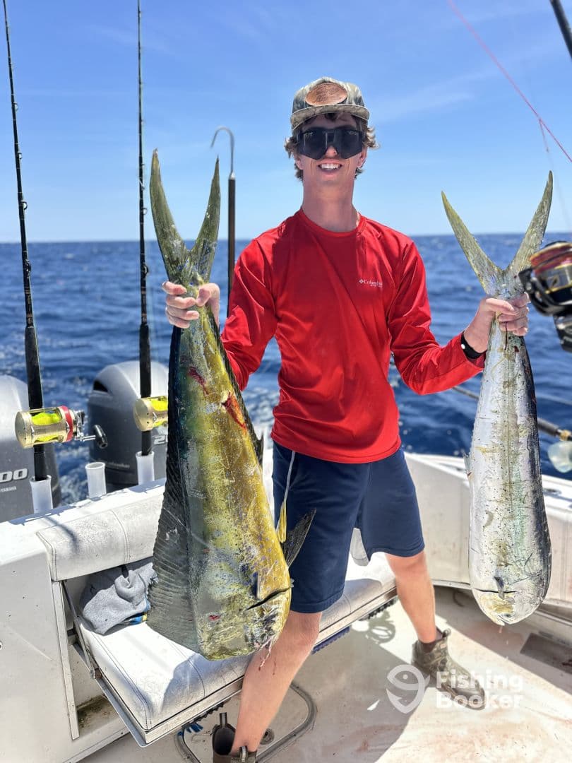 A young angler proudly displaying two vibrant Mahi Mahi while fishing offshore, showcasing a successful day on the water.