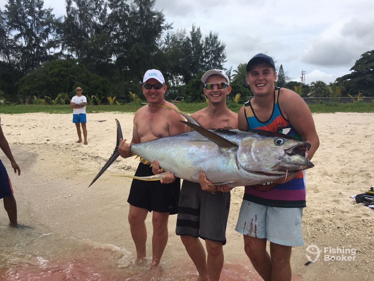 Three anglers proudly displaying a large Yellowfin Tuna on the beach after a successful fishing trip.