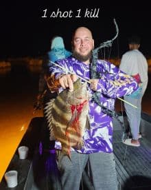 Angler proudly displaying a large striped fish caught at night, showcasing the excitement of bowfishing.