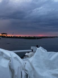 A serene view of the boat's side with a dramatic sunset backdrop, showcasing the calm waters and cloudy sky.