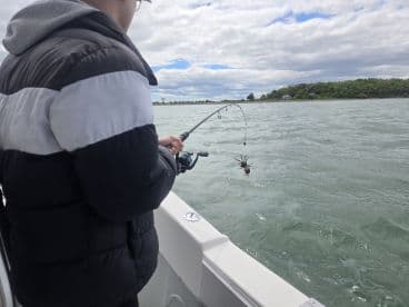 A young angler is reeling in a catch while fishing from a boat, showcasing an exciting moment on the water.