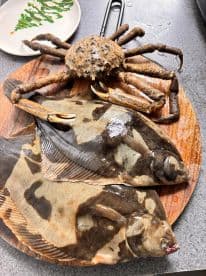A selection of freshly caught fish, including two flounders and a crab, displayed on a wooden cutting board, highlighting a successful fishing trip.