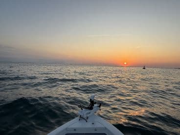 A serene sunset view from the front of a boat, showcasing calm waters and a picturesque horizon, ideal for evening fishing trips.